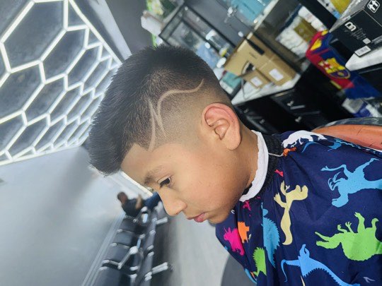 Niño con skin fade alto y una línea rapada en curva en el lateral.