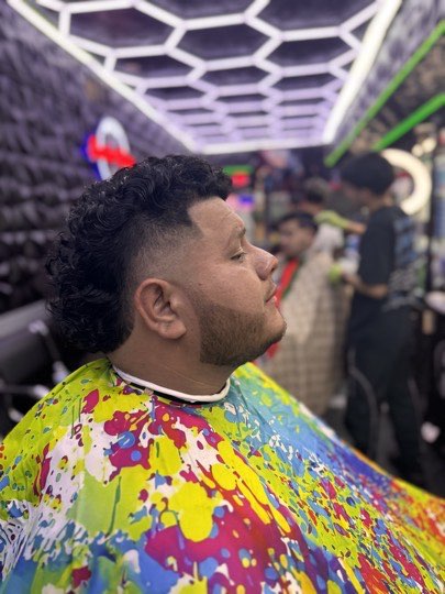 Curls on top with a mid fade and a lined up beard.