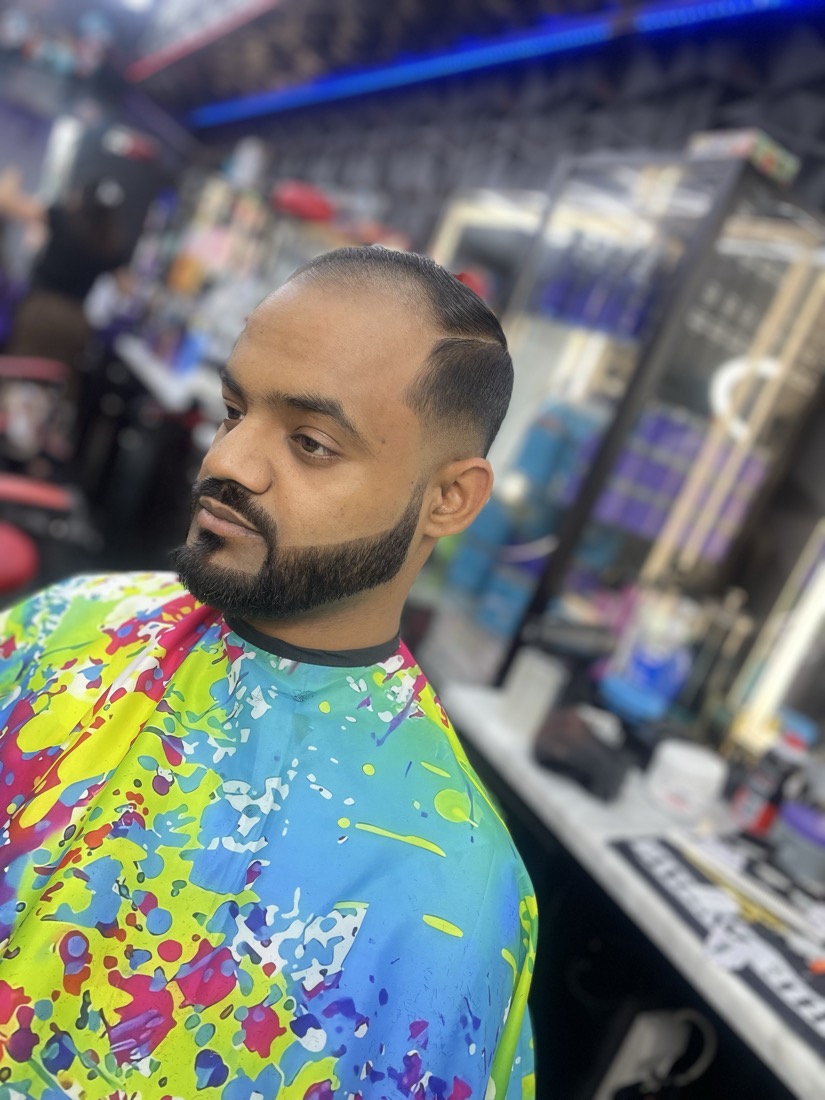 Skin fade con barba completa y perfilado en la frente.