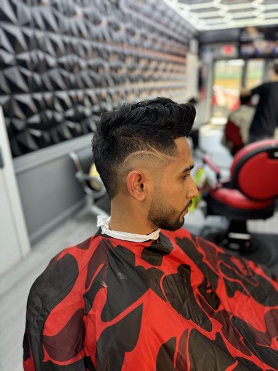Skin fade with the part shaved in with a razor, a quiff on top and a lined up beard.
