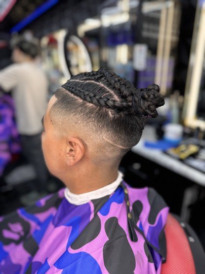Braids pulled up top with a skin fade and a shaved line on the side.
